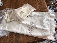 Full view of folded cream linen tablecloth with lace edging and a stack of six matching napkins on a wooden table.