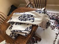 Four folded curtain panels on wooden dining table showing beige fabric with dark blue floral pattern.
