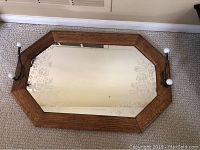 Top down photo of the octagonal mirror showing wood frame, etched floral patterns on glass, and hooks with ceramic knobs