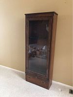 Front view of brown wood gun cabinet with glass door closed, showing overall shape and style