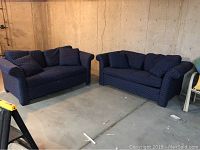 Two matching blue loveseats with small white polka dot pattern placed in basement on concrete floor.