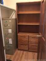Oak bookcase with four drawers and three shelves placed next to a metal file cabinet in an office closet.