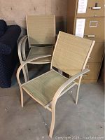 Photo showing two outdoor patio chairs stacked with beige/tan metal frames and mesh seats and backs.
