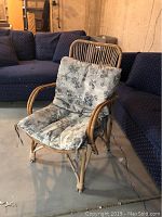Full view of rattan chair with cushions in a room with carpet and blue upholstered sofas nearby.