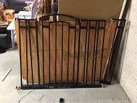 Photo showing the full gate laying against a beige wall in a storage or garage-like space, showing metal frame and wood panel.