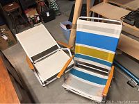 Two vintage folding beach chairs with white, blue, yellow, and teal striped fabric, aluminum frames, and wooden armrests.