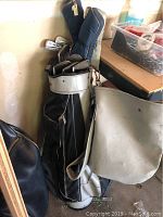 Overall view of white and black golf bag holding clubs with shoulder strap, standing upright in room corner