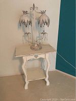 White wooden decorative table with curved legs and heart cutout on apron, shown with double-arm decorative table lamp with leaf-shaped metal lampshades and hanging crystal beads.