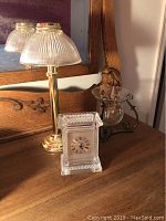 Crystal table clock and brass candleholder with ribbed glass shade photographed on wooden table with mirror background.
