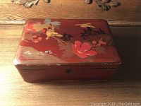 Top view showing red lacquer box with bird and flower painted design and minor paint wear.