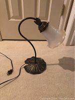 Full view of lily pad shaped metal base, curved stem and frosted glass shade.