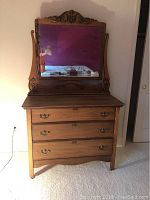 Front view of antique wooden chest of drawers with three drawers and attached mirror frame.