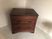 Front angled view of a wooden file cabinet showing two drawers with metal handles and slanted top with cable holes.