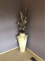 Full view of the large decorative urn with tall artificial flowers arranged inside.