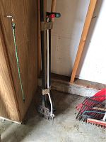 Long-handled metal rake and handheld weeding tool leaning against wall.