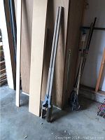 Full length view of both handle rods and metal digging blades standing upright indoors against a wooden background.