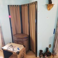 Three-panel dark wood framed room divider with gold fabric panels, standing upright in a room corner with surrounding furniture and decor.