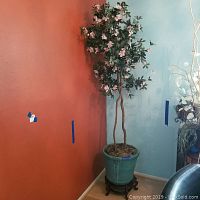 Cherry blossom faux tree with intertwined trunks, green leaves, light pink flowers in green pot on wooden stand.