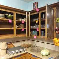 Open wooden kitchen cabinets with shelves containing assorted glassware and cups. Various basket and kitchen items on counter below including a silver case and a ceramic pumpkin container.