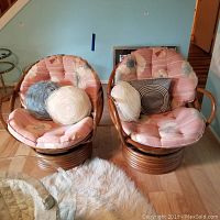 Two matching bamboo swivel chairs with floral striped cushions and accent pillows, placed on light wooden flooring by a wall painted light blue.