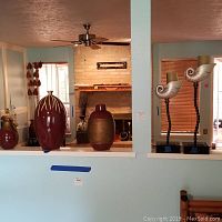 Photo of four decorative items on ledge: two red ceramic vases and two sea shell candle holders on stands