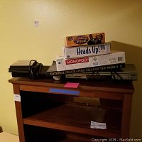 Photo of Samsung DVD player with board games and National Geographic Atlas stacked on top, placed on a wooden table