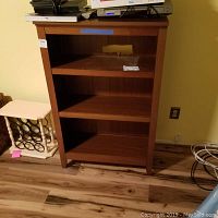 Front view of the wooden bookcase with three shelves and a visible cutout hole on the back panel.