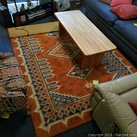 Orange and blue 5ft by 7ft rug placed on floor under coffee table, visible wear is minimal.
