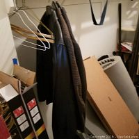 Multiple men's jackets hanging in a closet, including a distinct Wilson's leather jacket in front and several men's fabric suit jackets behind.