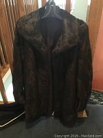 Full view of dark brown short fur coat on hanger showing front with collar and long sleeves