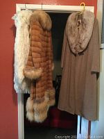 Three women's coats hanging: white Saks Fifth Avenue fur coat, brown Roberts Furs fur coat, camel Regency cashmere coat with large collar