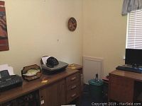 Desk with black Dell printer model A920, black HP 1040 fax machine, push button office phone, Billy Bass musical fish, cords, and papers on wooden drawers.