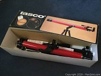 Photo of the unassembled red Tasco telescope tube and tripod components inside the original box, showing the instruction booklet included.