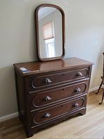 Front view of dark wood dresser with three drawers and a separate standing mirror on top.