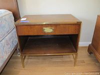 Front view of the Baker Furniture wooden bedside table showing drawer, open shelf, and metal legs.
