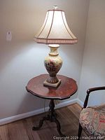 Photo of the round wooden pedestal table with lamp placed on top showing full table and upper portion of the lamp.