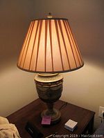 Photo of the first decorative table lamp with urn-shaped ceramic base and brown striped lampshade turned on, showing lamp fully assembled and lit.
