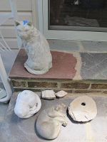Three cat statues and three rocks arranged on a stone surface with a brick step in background.