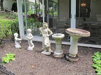 Front view of all items arranged outdoors showing three statues, bird baths, and sundial.