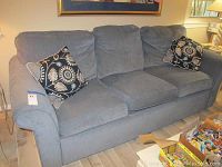 Grey fabric sofa with three seats, attached back cushions, and two black and beige patterned throw pillows. Sofa shows wear and pet scratches.
