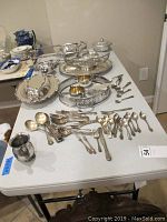 Full assortment of silverplate utensils and serving pieces displayed on table including spoons, forks, platters, bowls, sugar bowl, and creamer.