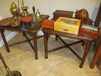 Two wood side tables with glass tops, bamboo-style wood legs, and cross supports seen with various items on top.