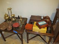 Overall view of glass table with metal decor including brass urn, pitcher, bell, hourglass on left side and wooden boxes and elephant bookends on right side.
