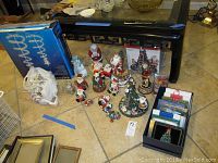 Photo showing assorted Christmas figurines, Santa figures, a conical Christmas tree, a box of cards, and original box for string lights