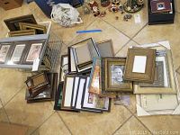 Photo showing a large number of assorted empty picture frames on floor with a few decorative items in distance