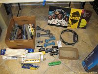 Photo showing vinyl records, dumbbells, tambourine, harmonica, and miscellaneous items on floor with cardboard box containing various small objects.