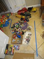 Lot overview showing scattered toys including trucks, cars, planes, figures, and polished stones on tiled floor
