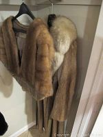 Mink shrug and long nutria coat hanging side by side showing overall shape and fur detail.