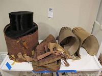 Antique black beaver top hat, two old bonnets, quilted hood, and vintage hat box displayed on table.