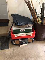 Photo showing stacked items including the red Little Tikes wagon at the bottom, a green Coleman cooler on top, and multiple air mattresses folded and placed above the cooler